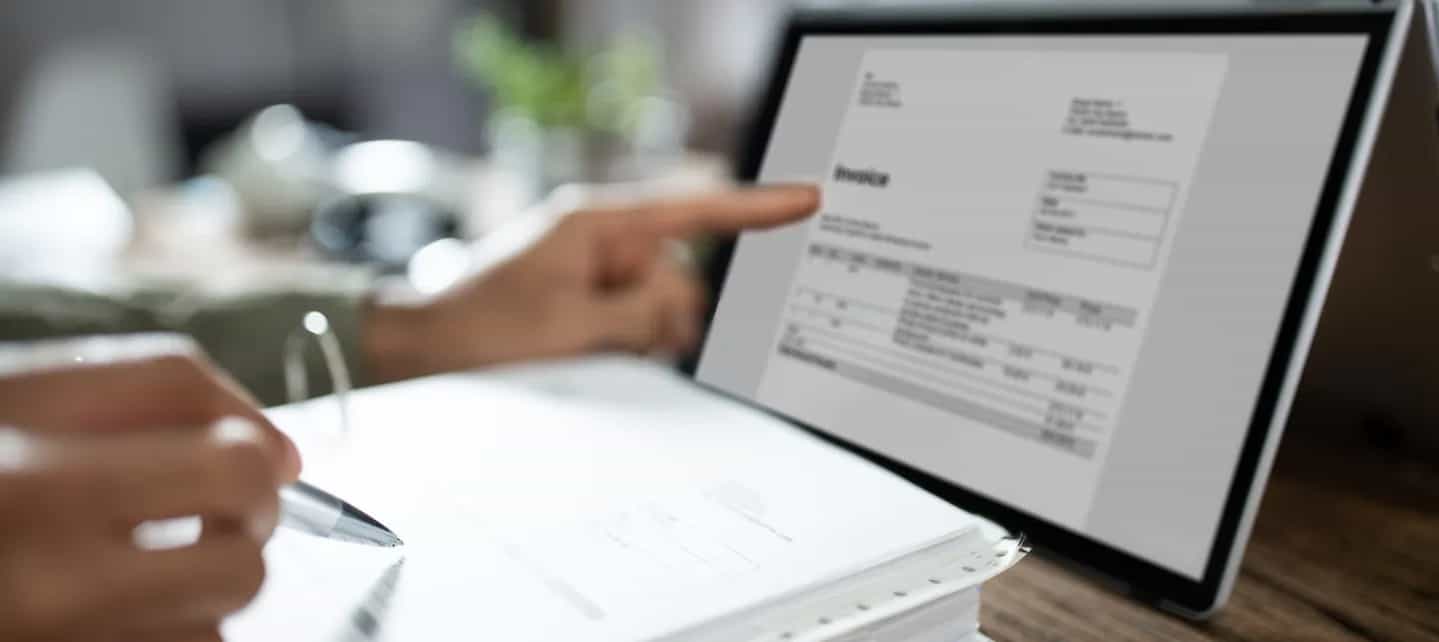 En hånd som skriver på et ark foran et nettbrett 