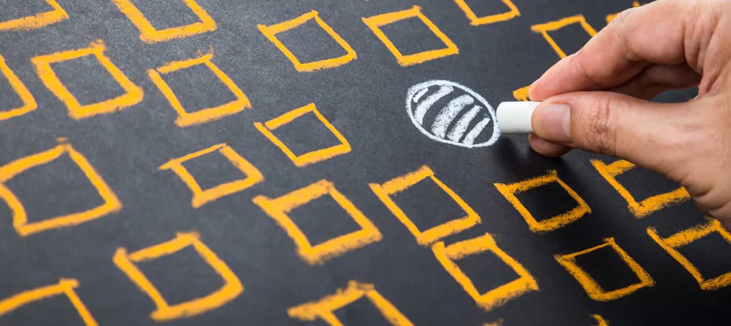 Hånd med kritt som streker over en hvit sirkel, omringet av gule bokser på en tavle