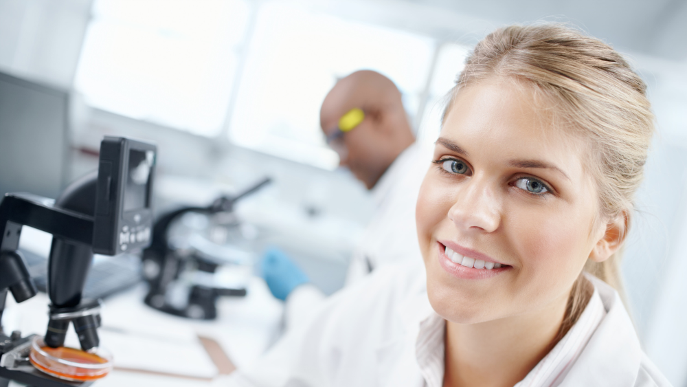 Kvinnelig forsker med hvit frakk og mikroskop