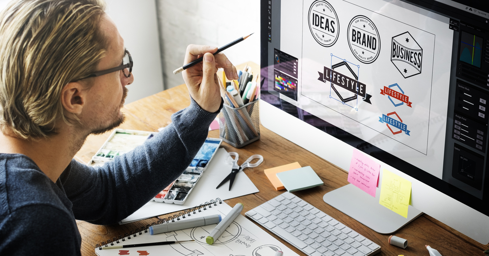 Mann som peker på en pc-skjerm med logoer, som viser ord som: Ideas, Brand og Lifestyle